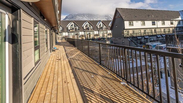Eine Holzterrasse mit Metallgeländer, mit Blick auf eine Häuserreihe vor einer Bergkulisse.