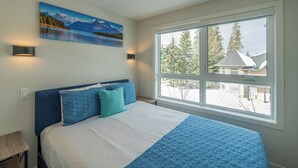 Ein Schlafzimmer mit einem großen Bett, einem Fenster mit Blick auf Bäume und ein Haus, sowie einem Gemälde eines Sees an der Wand.