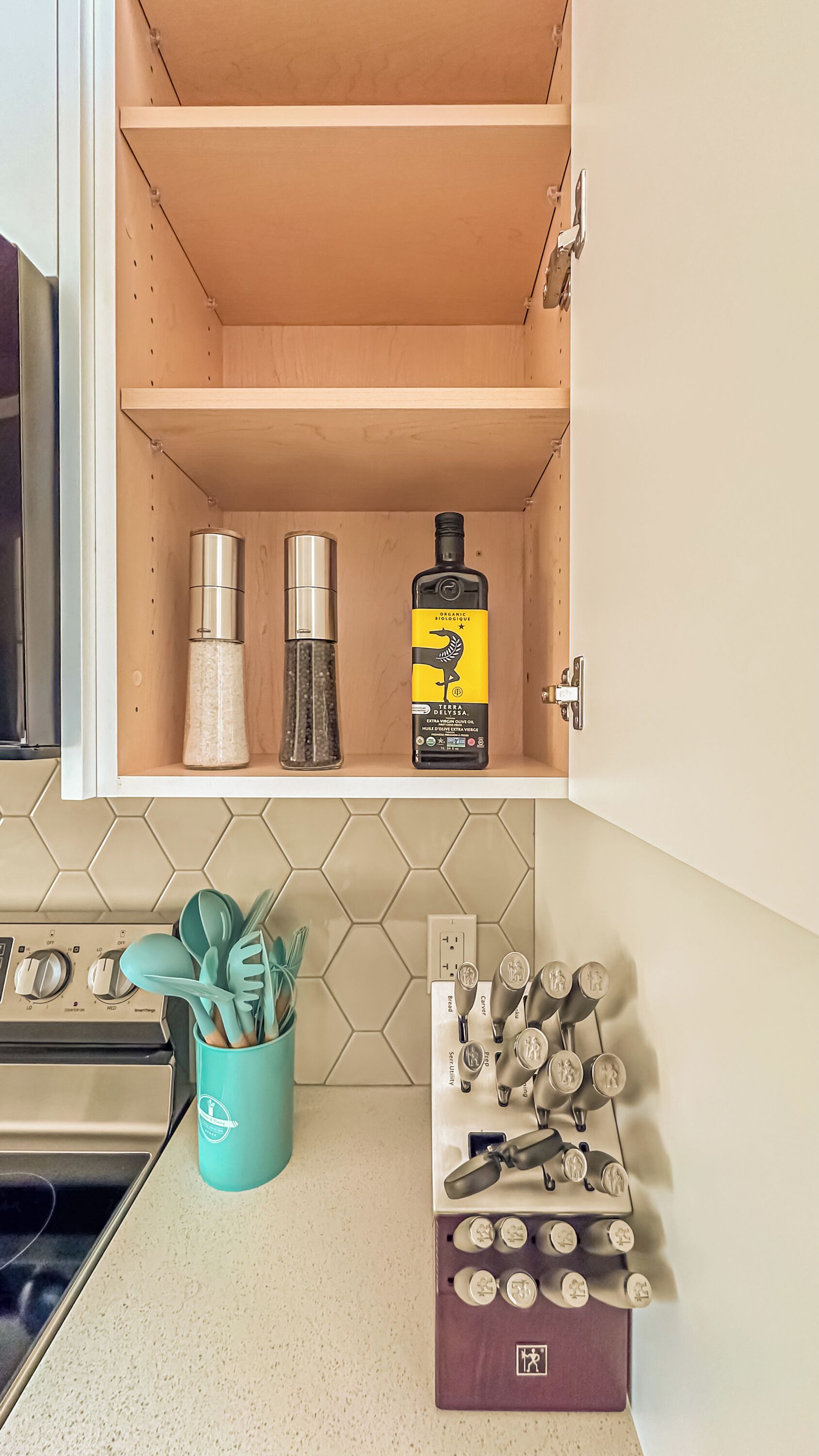 A kitchen cabinet with a honeycomb tile backsplash, a teal utensil holder, and a spice rack with labeled containers.