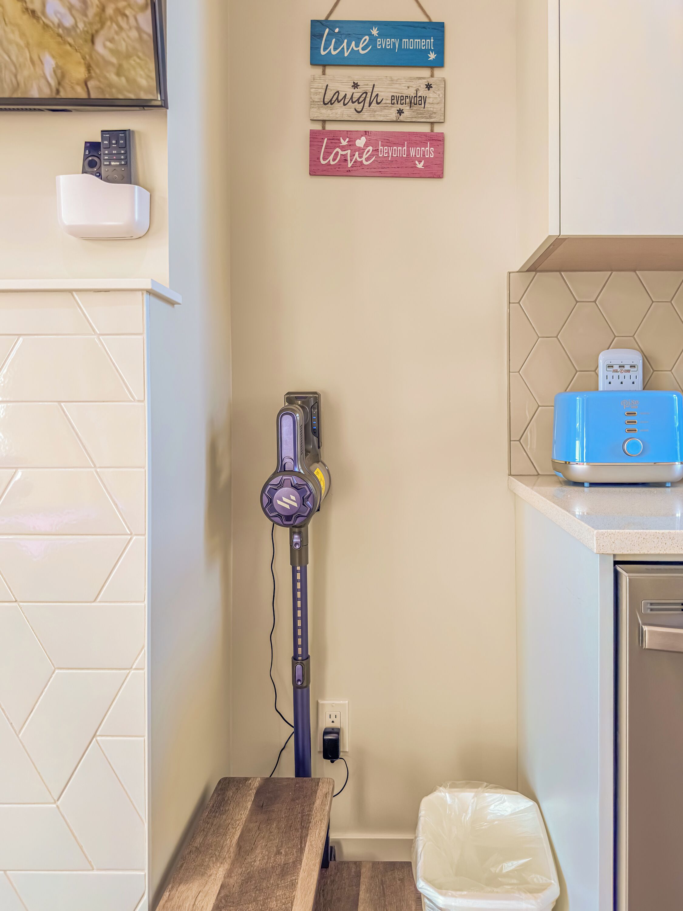 Une cuisine équipée d’un aspirateur, d’une multiprise fixée au mur et d’un plan de travail sur lequel se trouve un appareil électroménager bleu.