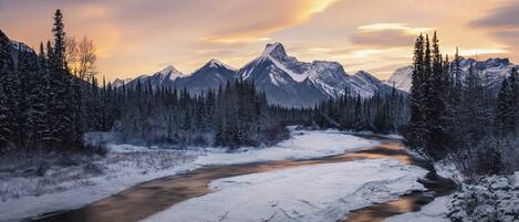 A snow-covered river flowing through a forest with mountains in the background.