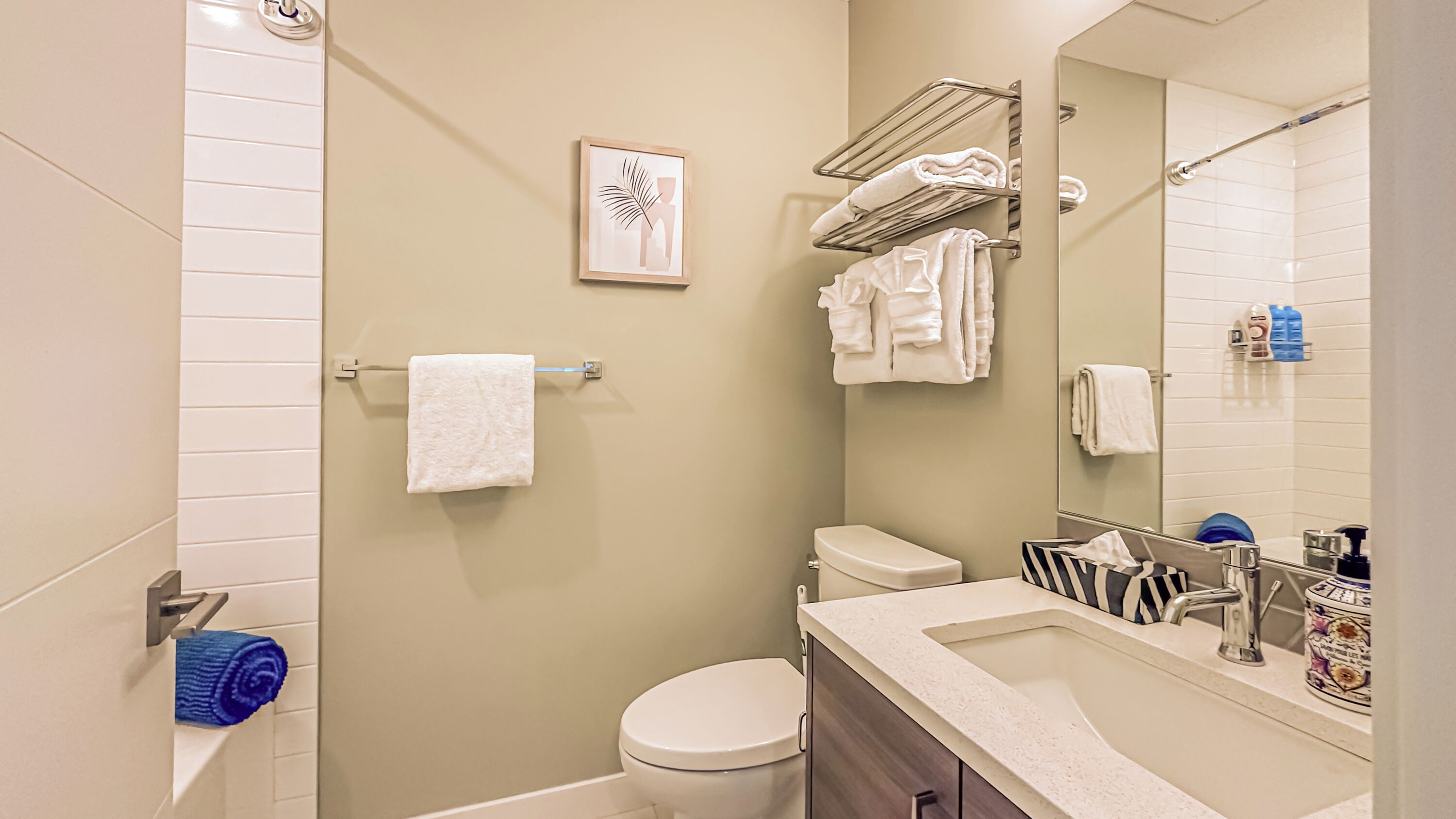 Une salle de bain moderne avec des toilettes, un lavabo et une douche. On y trouve des serviettes sur un porte-serviettes et un tableau encadré au mur.