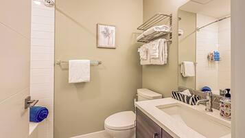 Une salle de bain moderne avec des toilettes, un lavabo et une douche. On y trouve des serviettes sur un porte-serviettes et un tableau encadré au mur.