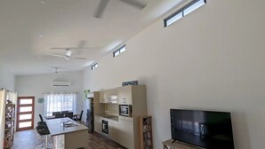 Eine moderne Küche mit Kochinsel, Essbereich mit Stühlen, Fernseher auf einem Schrank und Deckenventilator.