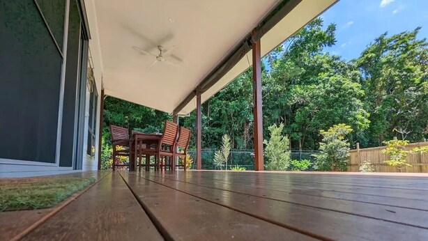 Eine Holzdielen-Terrasse mit Deckenventilator, Tisch und Stühlen, und Blick auf üppiges Grün.
