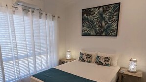Ein Schlafzimmer mit einem Bett, einem Deckenventilator, einer Wand-Klimaanlage, einem Fenster mit Vorhängen und einem Nachttisch mit Lampe.