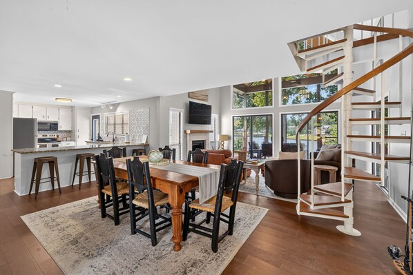 A spacious living area with a dining table, chairs, a fireplace, and a view of the outdoors. - Lakeshore Retreat- Lake Sinclair/Milledgeville (Milledgeville)