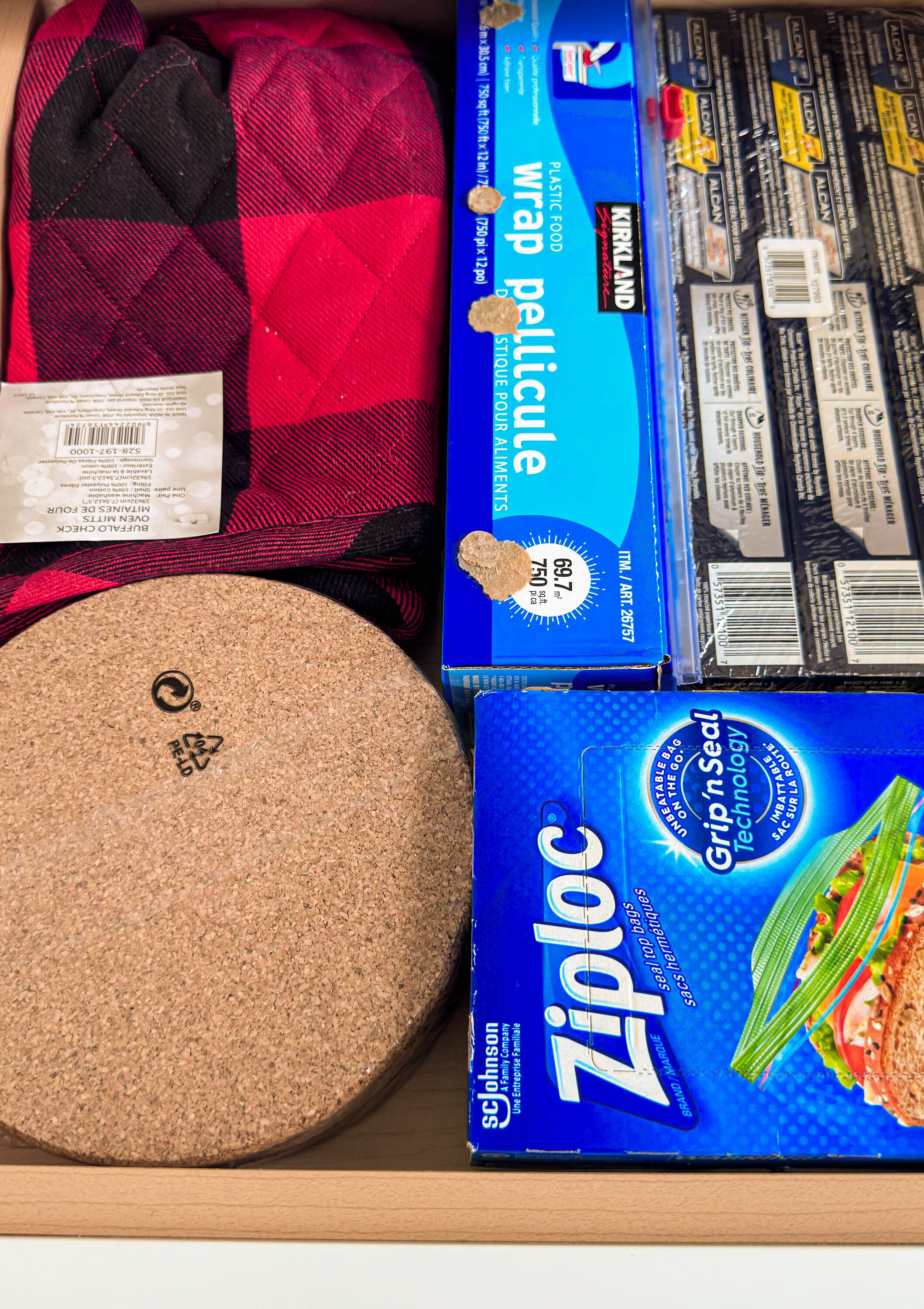 A storage box containing a cork mat, a red and black checkered bag, a plastic wrap package, and a Ziplock bag.