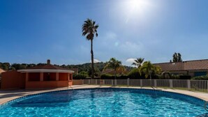 Una piscina azul cristalina con borde de azulejos, rodeada por una cerca blanca y palmeras.
