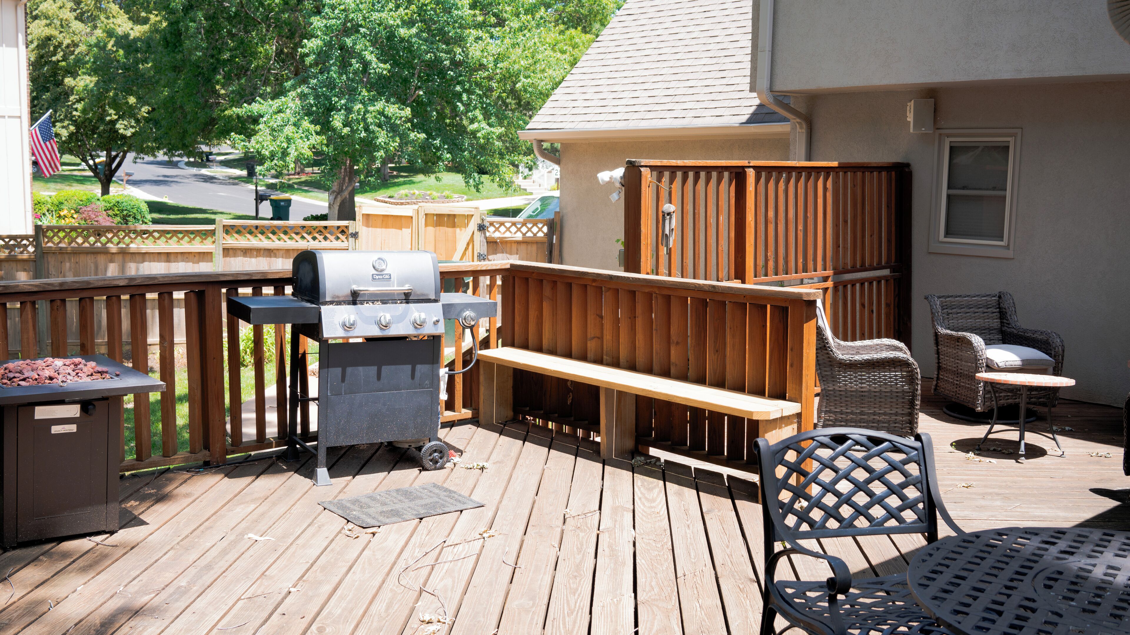 Una terraza de madera con una parrilla, zona de estar y mobiliario exterior.