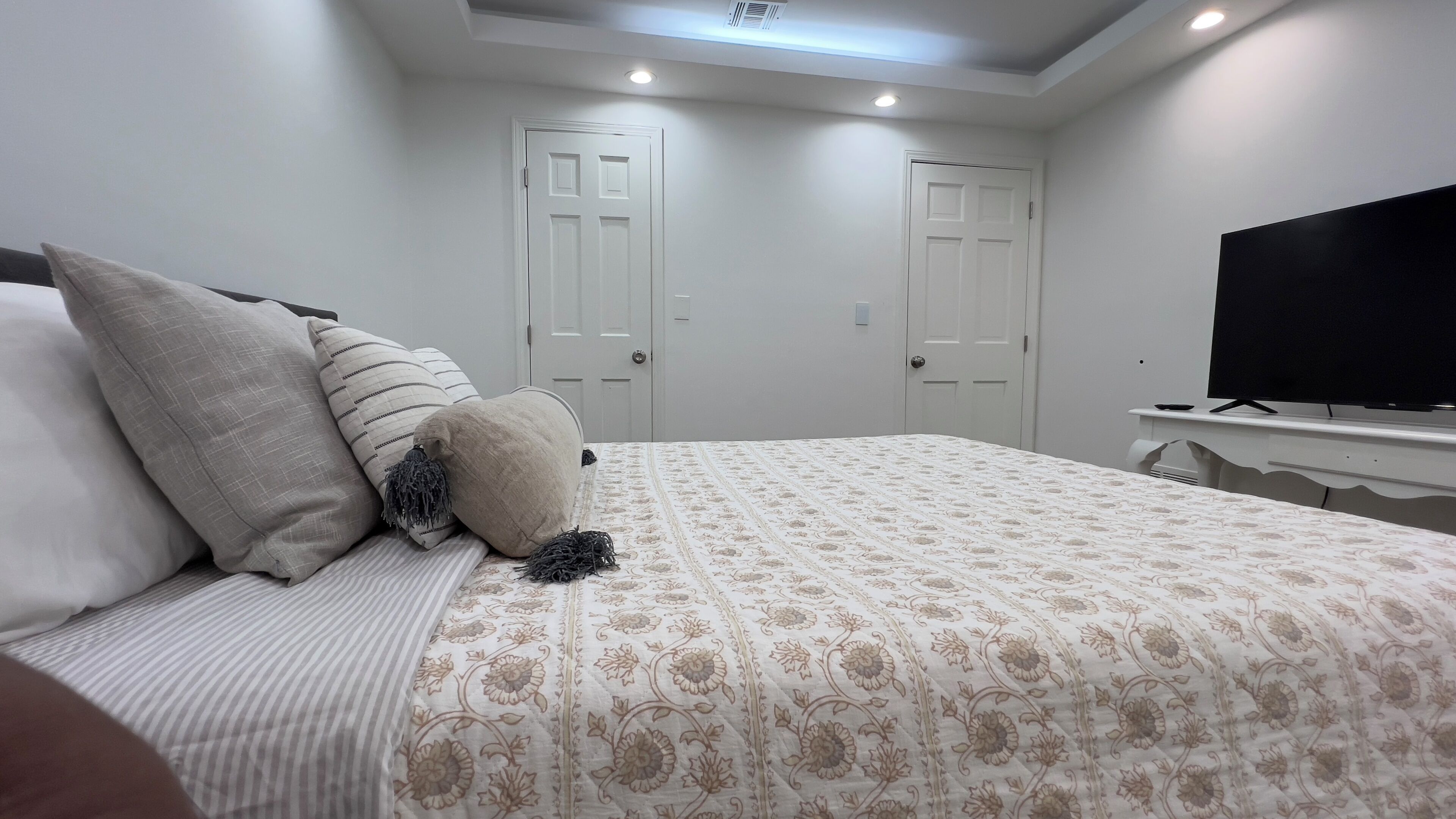 Une chambre à coucher avec un lit, deux portes, une télévision et un luminaire au plafond.