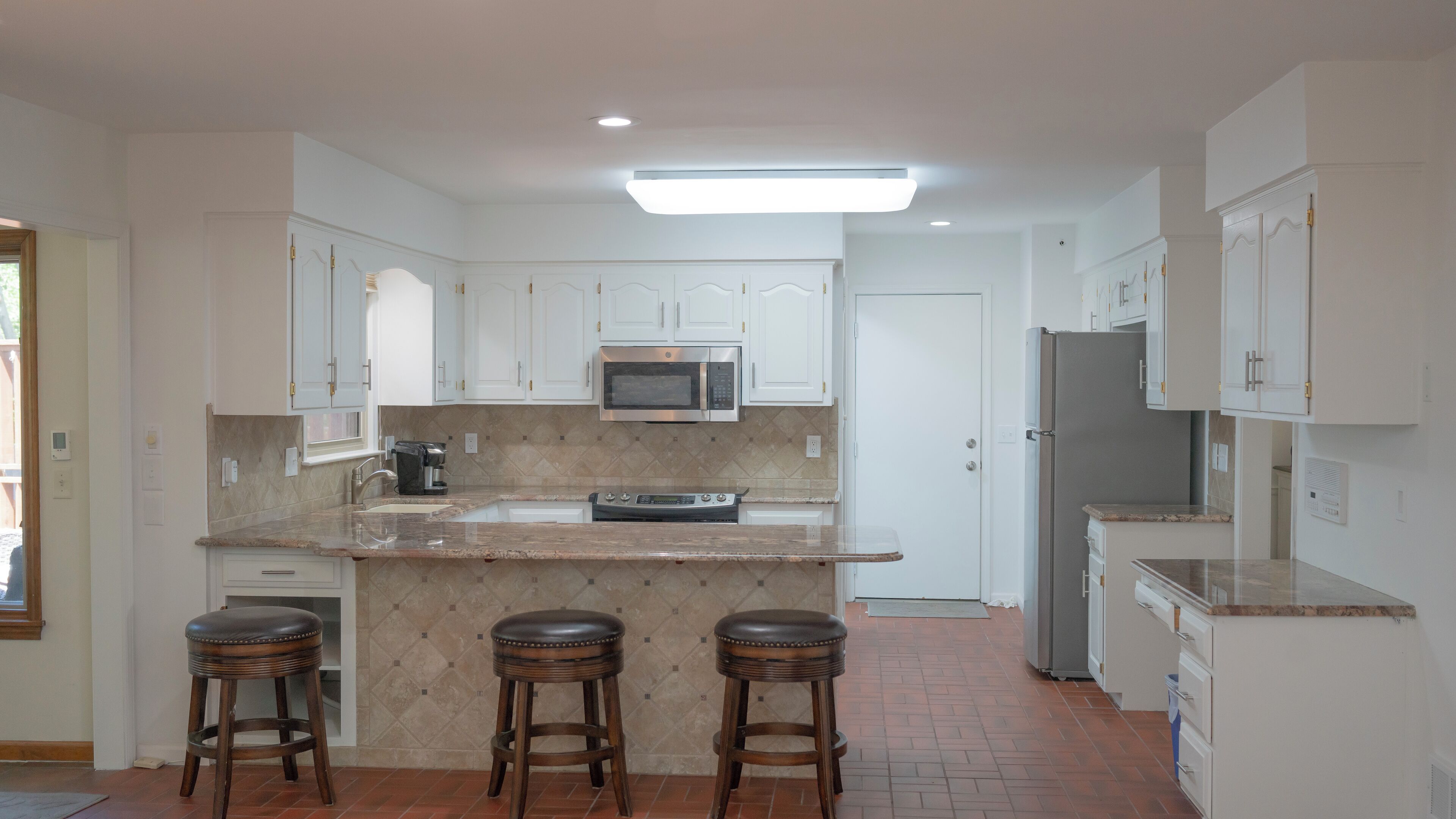 Una cocina moderna con armarios blancos, una isla central con taburetes, un microondas empotrado y un refrigerador.