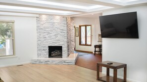 Un salon moderne avec une cheminée en pierre, un plancher en bois et un téléviseur à écran plat fixé au mur.