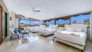 Un dormitorio amplio con dos camas, un sofá, un escritorio y grandes ventanas que dan a vistas de palmeras y el cielo.