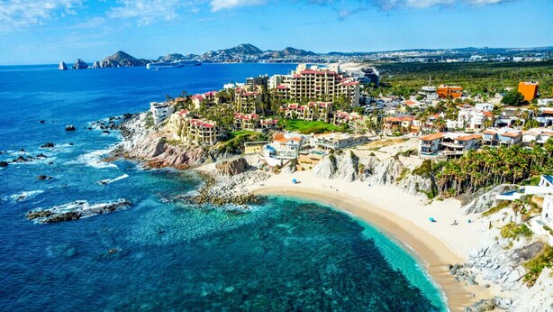 Un complejo turístico frente a la playa, con aguas cristalinas y diversas construcciones, incluyendo hoteles y villas.