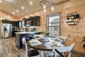 A modern kitchen with wooden walls, a central island, and a dining area with white chairs. - Heated Pool & 305Mbps Wi-Fi-No Winding Roads (Sevierville)