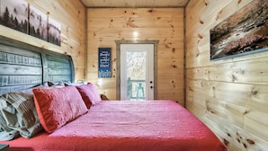 Quarto de cabana de madeira com cama, almofadas e porta que dá para uma varanda.
