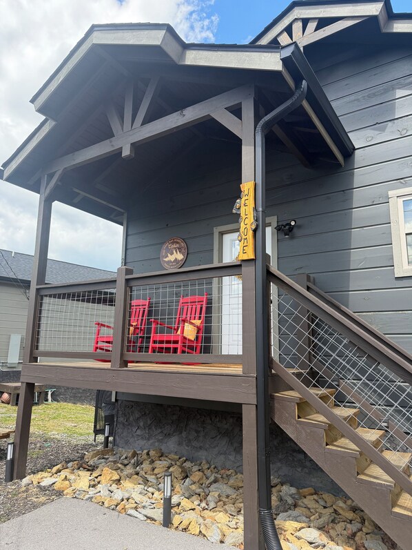 A wooden cabin with a porch, red chairs, and a welcome sign.