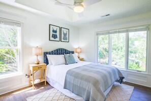 A bedroom with a bed, two bedside lamps, a ceiling fan, and large windows.