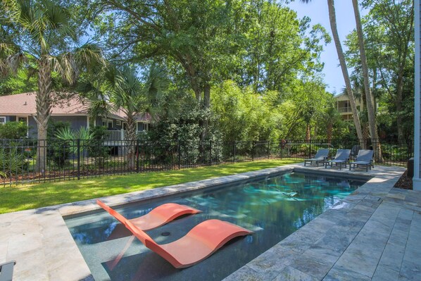 A swimming pool with lounge chairs and a fence.