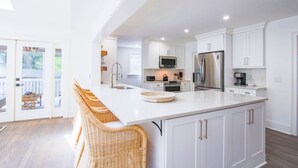 A modern kitchen with white cabinetry, a large island with bar stools, stainless steel appliances, and a view to the outside. - Relax in Renovated Home w/ Private Plunge Pool; Screened Porch; 2 Master Suites; 4 Min Walk to Beach (Isle of Palms)