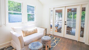 A bright room with a white sofa, two woven ottomans, and a large window. - Relax in Renovated Home w/ Private Plunge Pool; Screened Porch; 2 Master Suites; 4 Min Walk to Beach (Isle of Palms)
