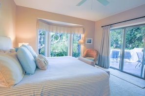 A bedroom with a large bed, a chair, a lamp, and a view of the outdoors through a sliding glass door.