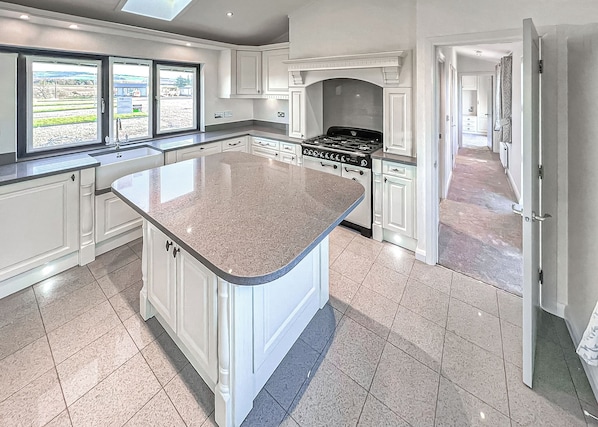 A modern kitchen with a large island, white cabinetry, a gas stove, and a view through the windows.
