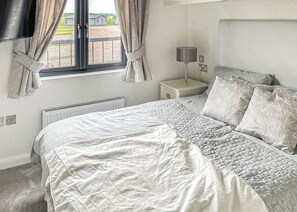 A bedroom with a large bed, a bedside table with a lamp, a window with curtains, and a radiator.