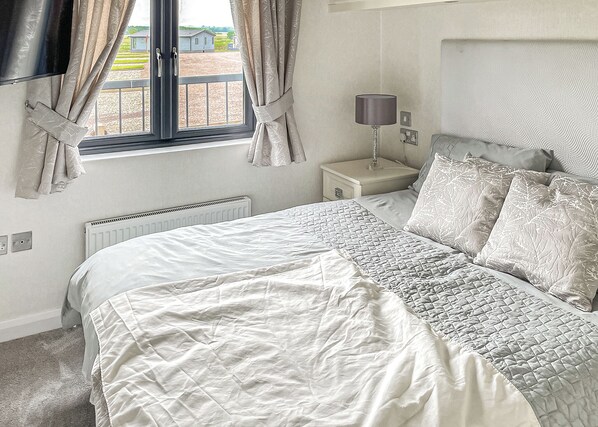 A bedroom with a large bed, a bedside table with a lamp, a window with curtains, and a radiator.