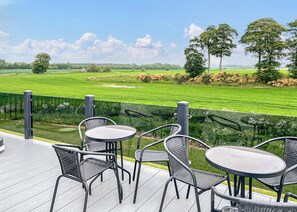 A deck with outdoor furniture overlooking a green field.
