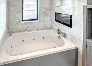 A modern bathroom with a large bathtub, a built-in TV, and marble walls.