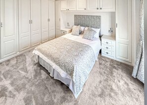 A bedroom with a large bed, white wardrobe, and a nightstand.