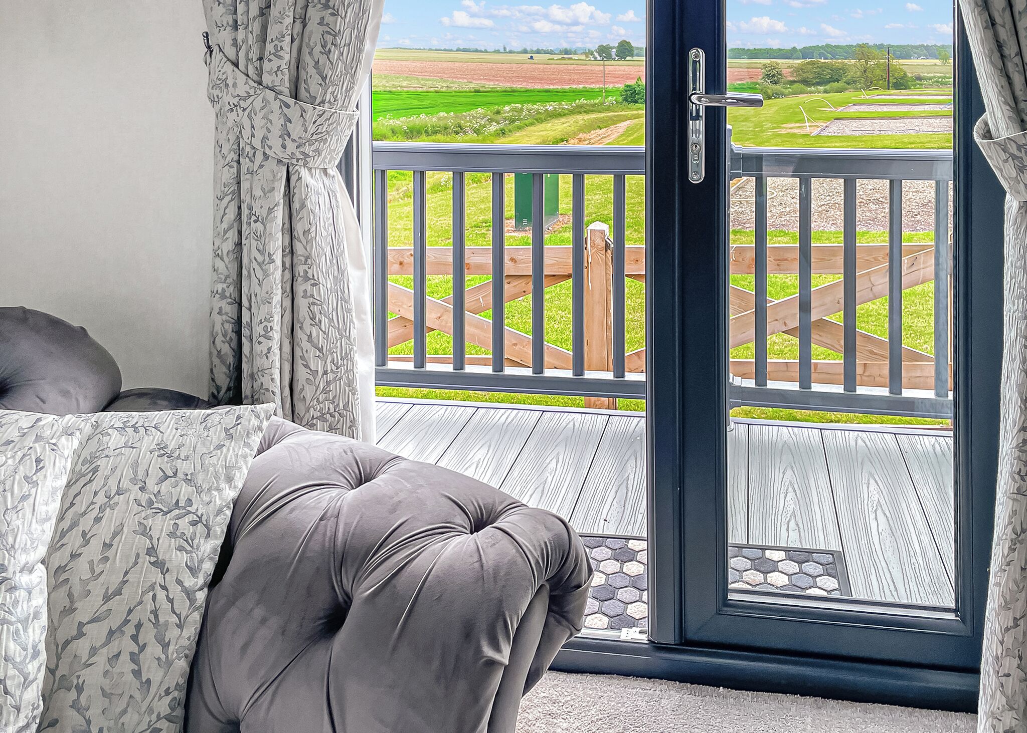 A balcony with a view of a green field, a wooden deck, and a door leading outside.