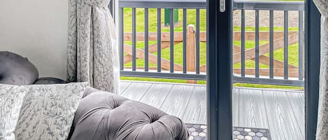 A balcony with a view of a green field, a wooden deck, and a door leading outside.