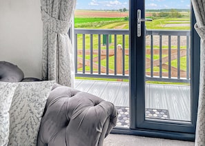 A balcony with a view of a green field, a wooden deck, and a door leading outside.