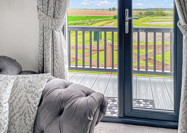 A balcony with a view of a green field, a wooden deck, and a door leading outside.
