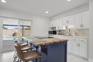 Enjoy meals in this kitchen with a central island, sink, and modern faucet, opening up to a patio with a pool view.