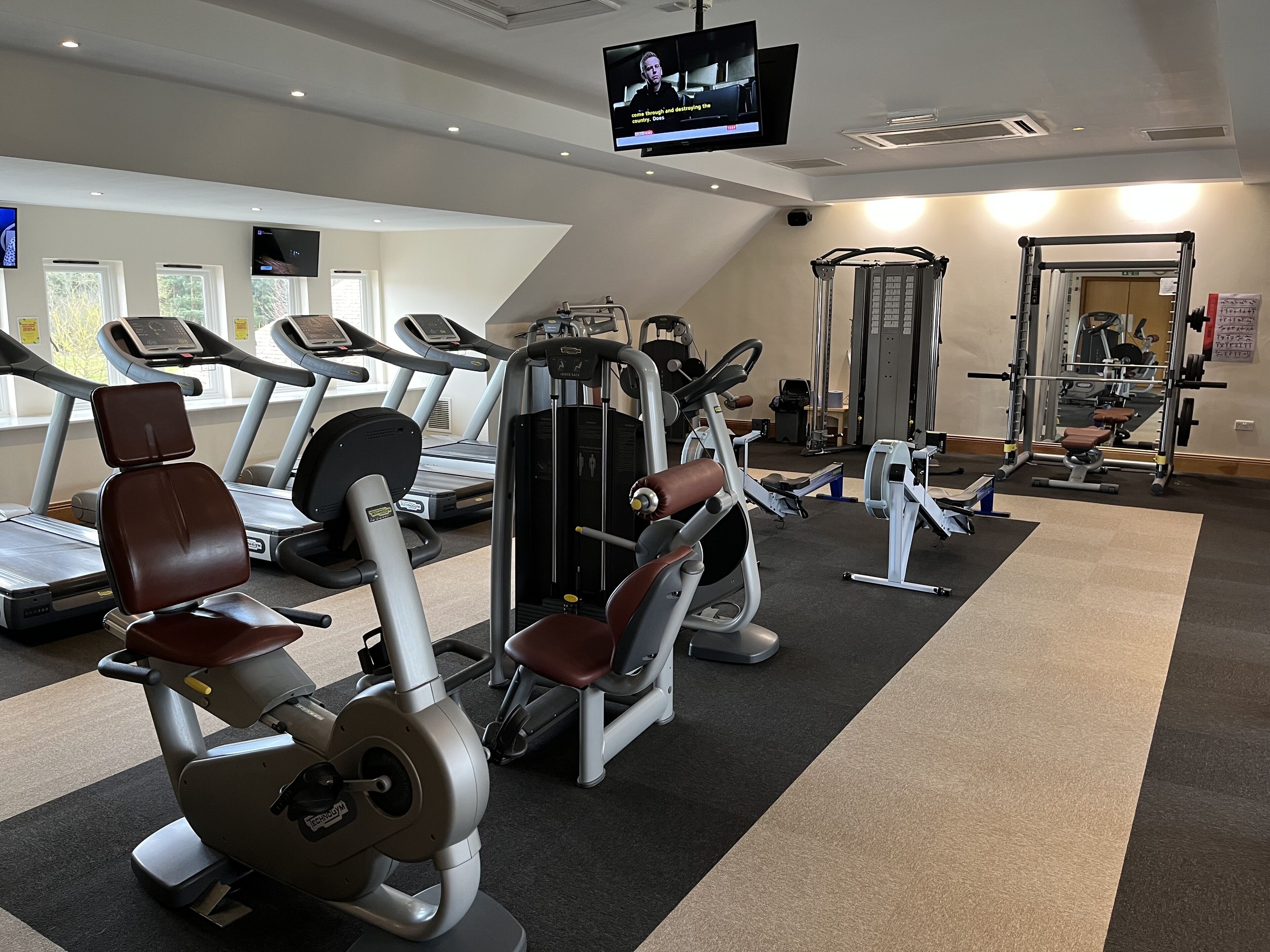 A gym with treadmills, weight machines, and a television screen.
