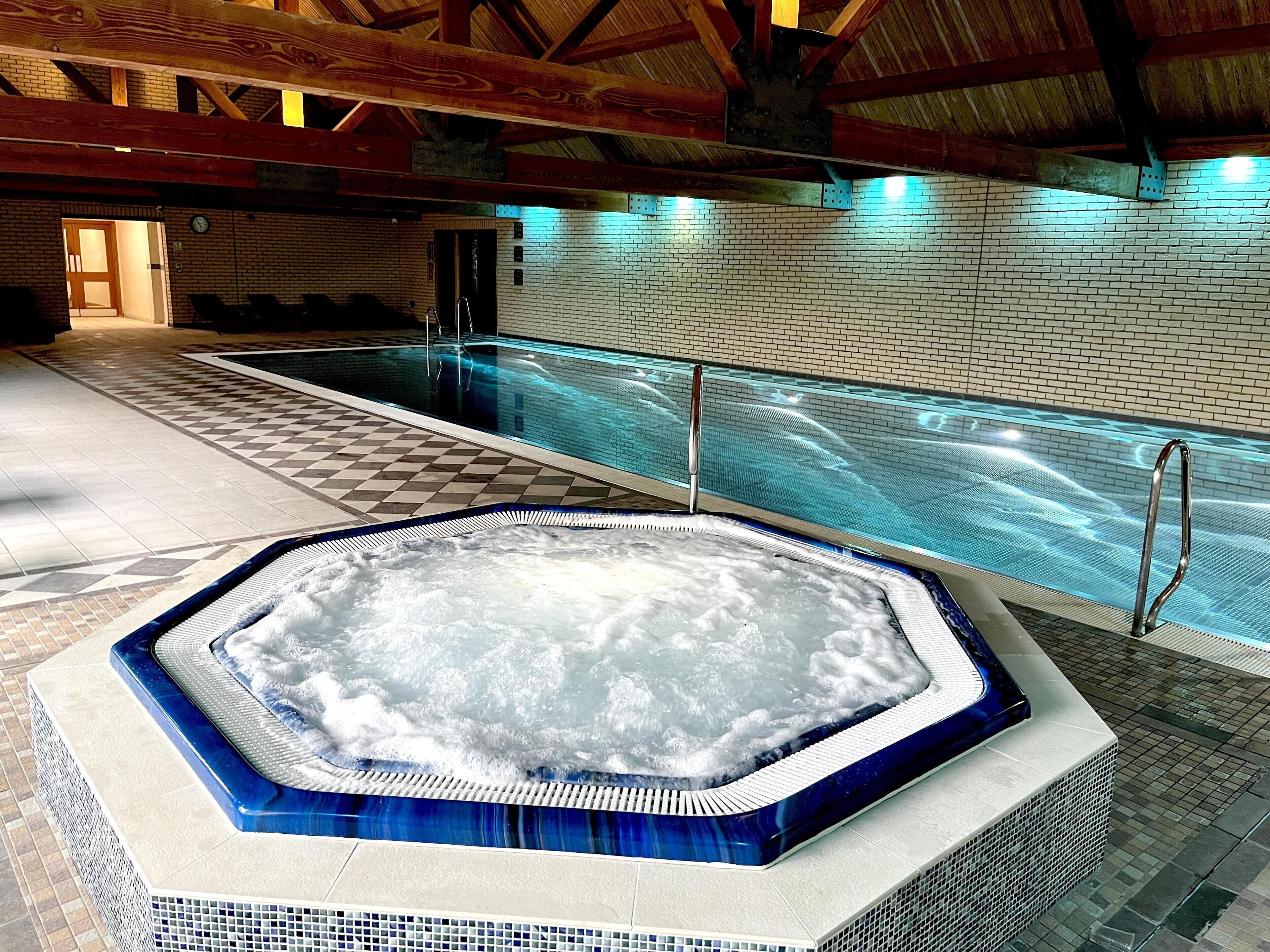Une piscine avec un jacuzzi, un revêtement de sol en carrelage et des poutres en bois au plafond.