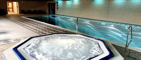 Une piscine avec un jacuzzi, un revêtement de sol en carrelage et des poutres en bois au plafond.