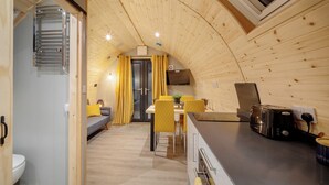 Un intérieur chaleureux avec un plafond en bois aux lignes courbes, un coin repas avec des chaises jaunes, une cuisine équipée d’un grille-pain et un petit coin salon avec un canapé.
