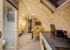 Un interno accogliente con soffitto in legno curvo, zona pranzo con sedie gialle, cucina con un tostapane e un piccolo angolo salotto con divano.