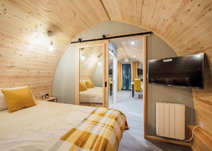 Un interior acogedor de madera con una cama, un televisor y una pared espejada que refleja otra habitación.