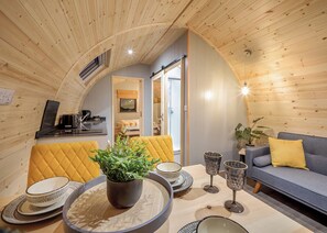 Un ambiente accogliente con soffitto in legno, un divano, un tavolo da pranzo con piatti e bicchieri, e una pianta.
