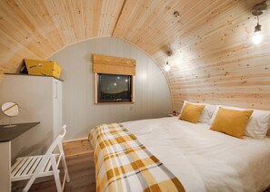 A cozy bedroom with a curved ceiling, a bed with yellow and white bedding, a small window, and a wooden desk with a chair.