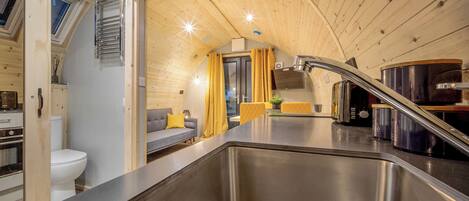 A compact kitchen with a stainless steel sink, wooden ceiling, and a sofa with yellow cushions.