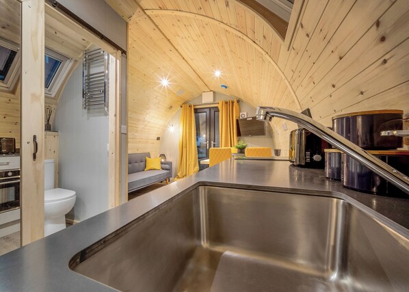 A compact kitchen with a stainless steel sink, wooden ceiling, and a sofa with yellow cushions.