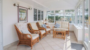 Una habitación soleada con muebles de mimbre, ventanas grandes y un cuadro en la pared.