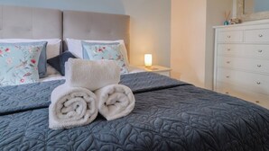 Una cama bien hecha con toallas enrolladas, una mesita de noche con lámpara y un aparador con cajones.